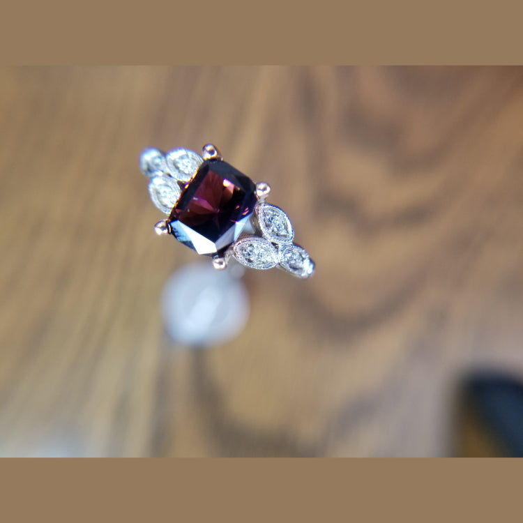 Custom 14k white and rose gold  tourmailine ring with diamond accents. The custom cut 2.07ct tourmaline that originated in Congo has a deep purplish pink color, and is set in a four prong rose gold head. The ring features a leaf style pattern on the shank with 7 round diamonds on each side.
