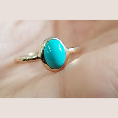 Beautiful custom ring features a 8 X 6mm oval turquoise is bezel set in a 14k yellow gold mounting, with a textured shank. The ring is a size 7.