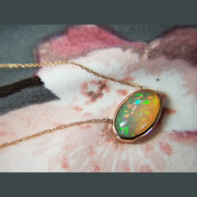 This stunning 14k rose gold pendant features a bezel set opal with vibrant hues of green. 